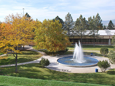 Photo of campus during fall including a fountain, lawn, and trees with green and yellow leaves