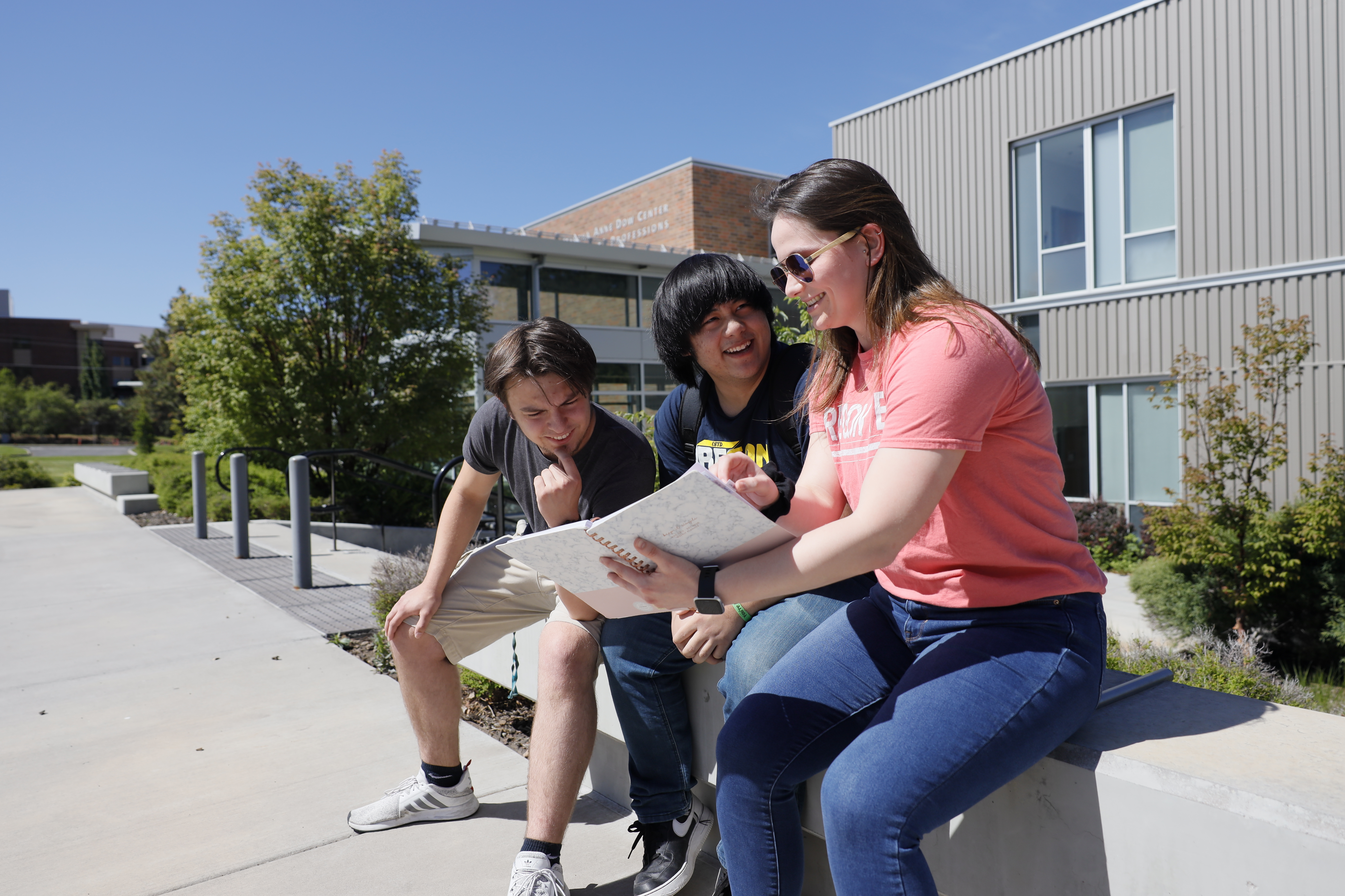 Students and counselor sitting on a low concrete wall talking, looking at information in a binder