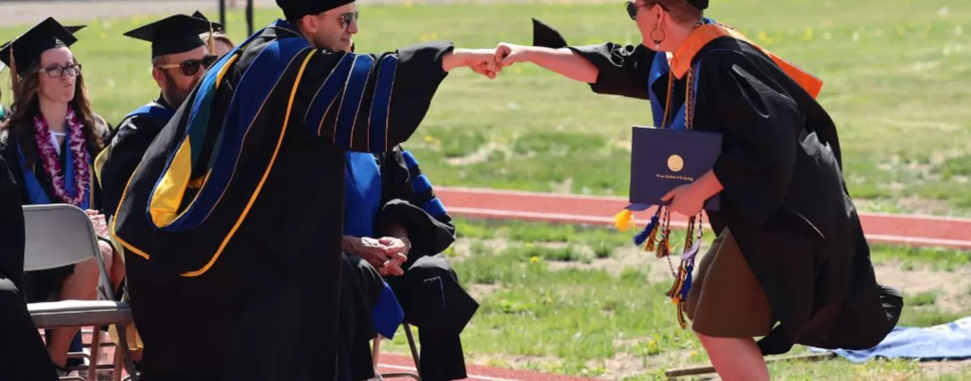 Faculty members fist bumps the graduating ASOIT student body president at commencement in 2022.