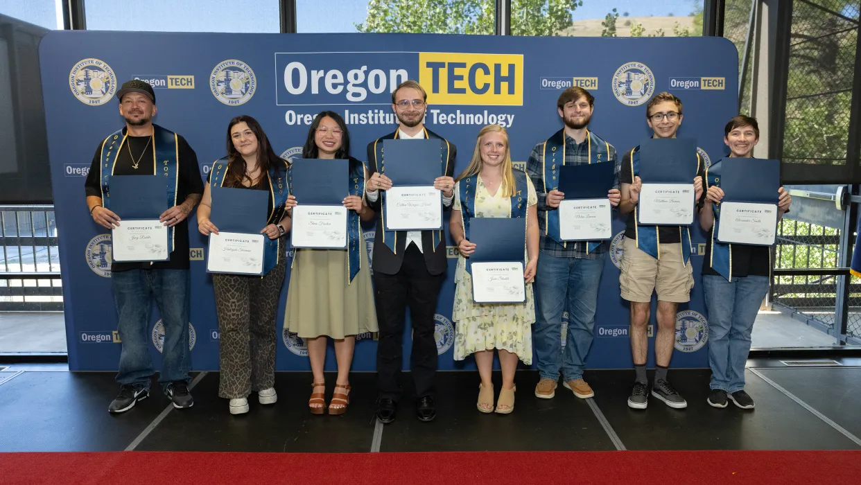 A group of TOP students posing in front of an Oregon Tech backdrop, while they proudly hold up certificates.
